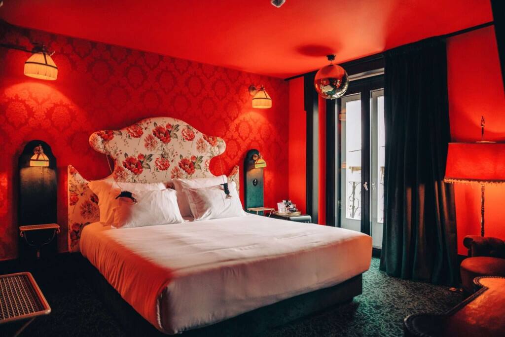 A softly lit vintage-style room in Madam’s Lodge at Pensao do Amor, designed like an old modern brothel, with velvet textures, red tones and antique details.