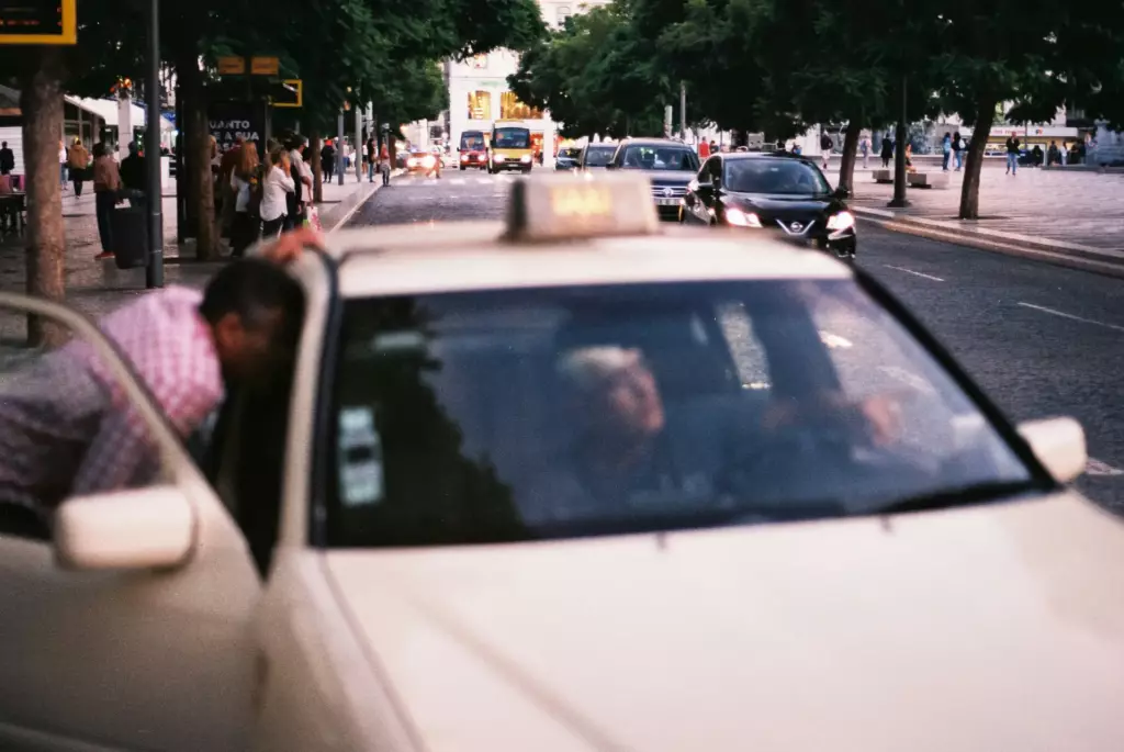 A man talking to a Lisbon taxi driver for advice while standing next to a yellow and black taxi.