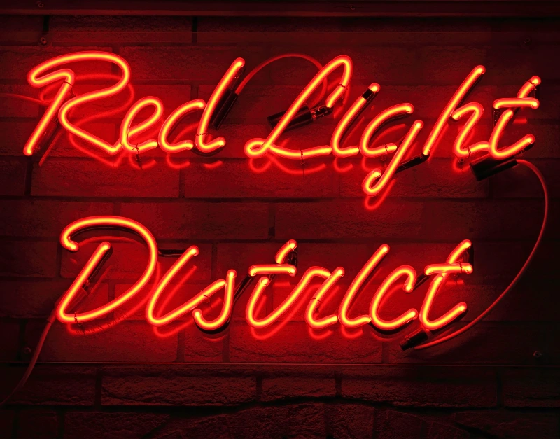 Red neon letters spelling red light district against a dark background